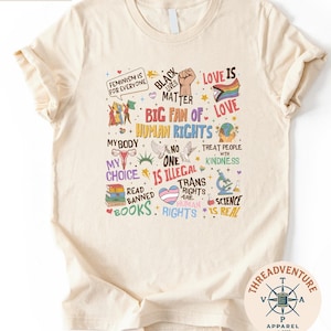 The image is a t-shirt with a collage of various colorful and diverse messages related to human rights, gender equality, and social justice.