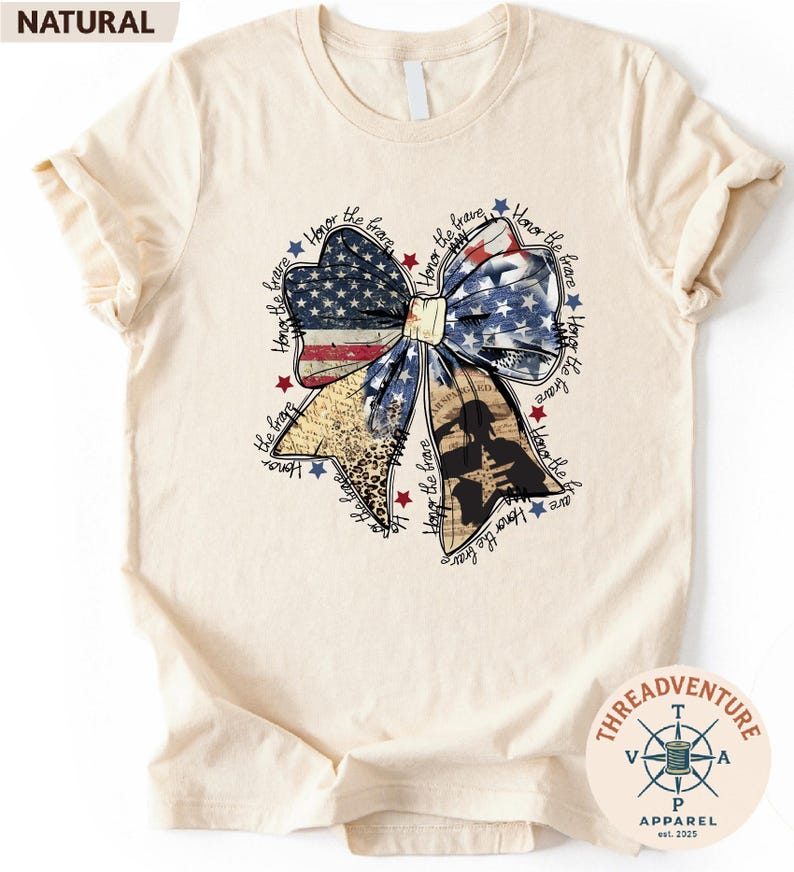 a white t-shirt with a graphic design depicting a large bow made up of various elements, including stars, stripes, and a flag. The bow is surrounded by text that appears to be a patriotic theme, possibly referencing American symbols and values.