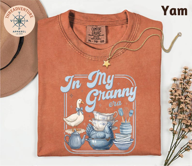 a red t-shirt with a graphic design of a duck and various kitchen items, including a teapot, bowls, and a star, along with the text "In My Granny era".