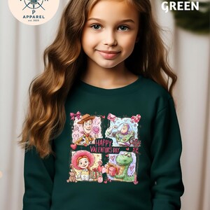 A young girl with long brown hair wearing a green sweater with a graphic design featuring characters from Toy Story.