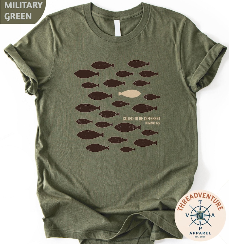 A military green t-shirt with a graphic design of a group of fish and a single fish in the center, along with the text "Called to be different" and "Bible verse 12:22".