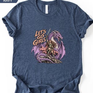 A navy blue t-shirt with a graphic design depicting a woman standing on a rock with a purple dragon behind her. The text on the t-shirt reads "Let's go girls".