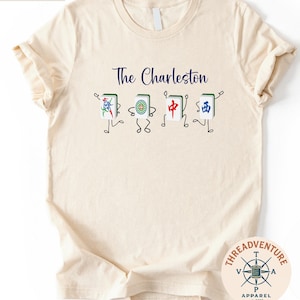 A beige t-shirt with a graphic design featuring four colorful, stylized characters that appear to be playing cards.