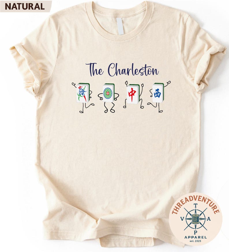A beige t-shirt with a graphic design featuring four colorful, stylized characters that appear to be playing cards.