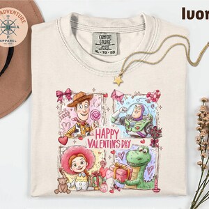 a white t-shirt with a colorful graphic design depicting characters from the Toy Story movie, including Woody, Buzz Lightyear, and a dinosaur. The design also includes the text "Happy Valentine's Day".