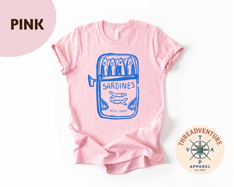 May include: A light pink t-shirt featuring a blue graphic of a sardine can with the word "Sardines" and the text "Wild Caught". The shirt has short sleeves and a crew neck. The Threadventure Apparel logo is in the bottom right corner.