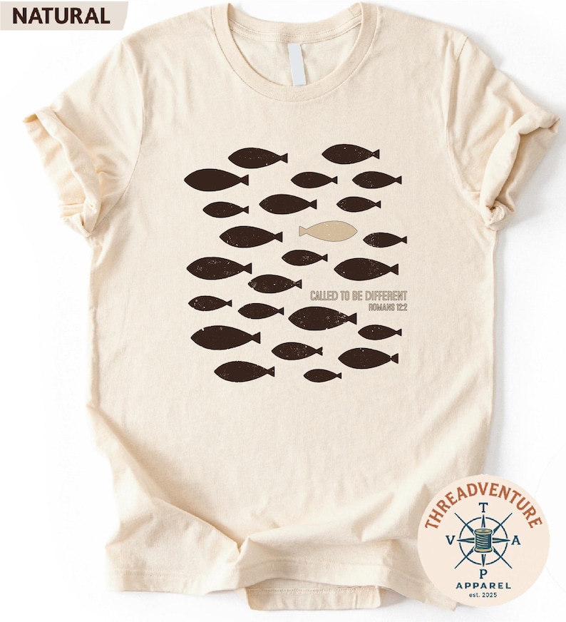 The image is a t-shirt with a graphic design featuring a group of fish, with one fish being different from the rest. The text on the t-shirt reads " Called to be Different" and "Roman 12".