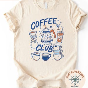 The image is a t-shirt with a graphic design featuring various coffee-related items such as a coffee pot, coffee cup, and coffee mug, along with the text "COFFEE CLUB" and the phrase "all every day".