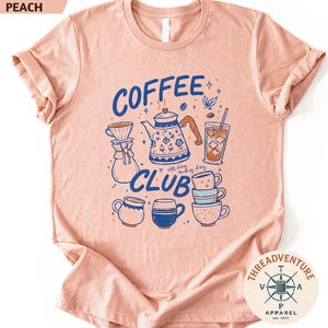 The image is a pink t-shirt with a graphic design featuring various coffee-related items such as a coffee pot, coffee cup, and coffee mug, along with the text "COFFEE CLUB" and "THREAD ADVENTURE APPAREL" printed on it.
