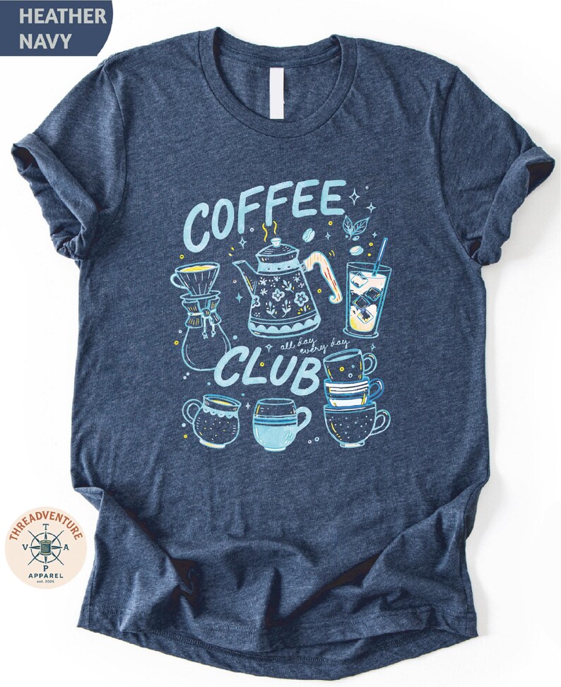 A navy blue t-shirt with a graphic design featuring various coffee-related items such as a coffee pot, coffee cups, and a teapot, along with the text "COFFEE CLUB" and other decorative elements.