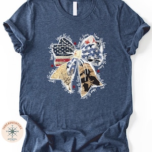 A navy blue t-shirt with a patriotic design featuring a large bow made up of various colors and shapes, including an American flag pattern.