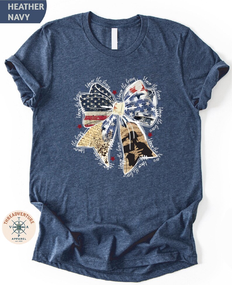 A navy blue t-shirt with a patriotic design featuring a large bow made up of various colors and shapes, including an American flag pattern.