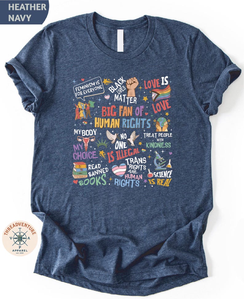 The image is a t-shirt with a collage of various texts and symbols related to human rights and social justice, including phrases like "Black is beautiful", "Love is love", "Big fan of human rights", "My body is my choice", "Treat people with kindness", "Read banned books", "Science is real", and "Trans rights are human rights".
