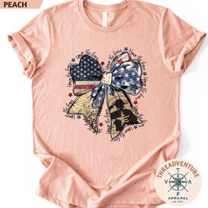 A pink t-shirt with a patriotic design featuring a large bow made up of American flag colors and stars.