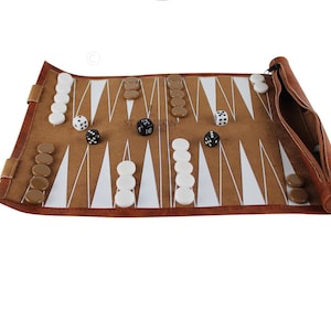 Peut inclure: Un jeu de backgammon en cuir marron avec des pions et des dés blancs et marron. Le plateau de jeu est ouvert, affichant la surface de jeu avec des triangles blancs et marron. L'ensemble est enroulé avec une fermeture éclair.