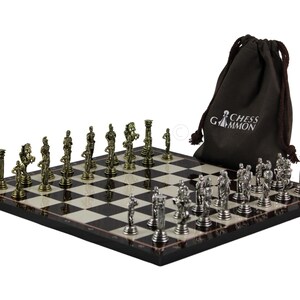 Könnte beinhalten: Ein quadratisches Schachbrett mit schwarz-weißem Karomuster und einem Satz metallischer, gold- und silberfarbener Schachfiguren. Ein dunkelbrauner Kordelzugbeutel mit dem weißen Schriftzug Chess Gammon befindet sich hinter dem Spielbrett.