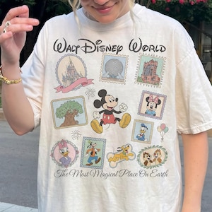 May include: Cream-colored Walt Disney World t-shirt featuring various Disney characters and park icons in a postage stamp design. The shirt includes Mickey Mouse, Minnie Mouse, Donald Duck, and Chip and Dale. Text reads "Walt Disney World" and "The Most Magical Place On Earth."