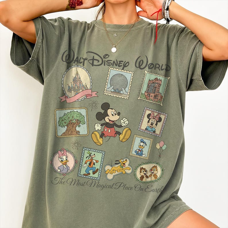May include: Olive green t-shirt featuring a Walt Disney World design. The shirt showcases various Disney characters and park icons within postage stamp-like frames. Text on the shirt reads "Walt Disney World" and "The Most Magical Place On Earth."