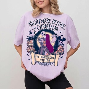 May include: A lilac t-shirt with a graphic from "The Nightmare Before Christmas." The design features Jack and Sally, pumpkins, bats, and the text "The Pumpkin King & Queen."