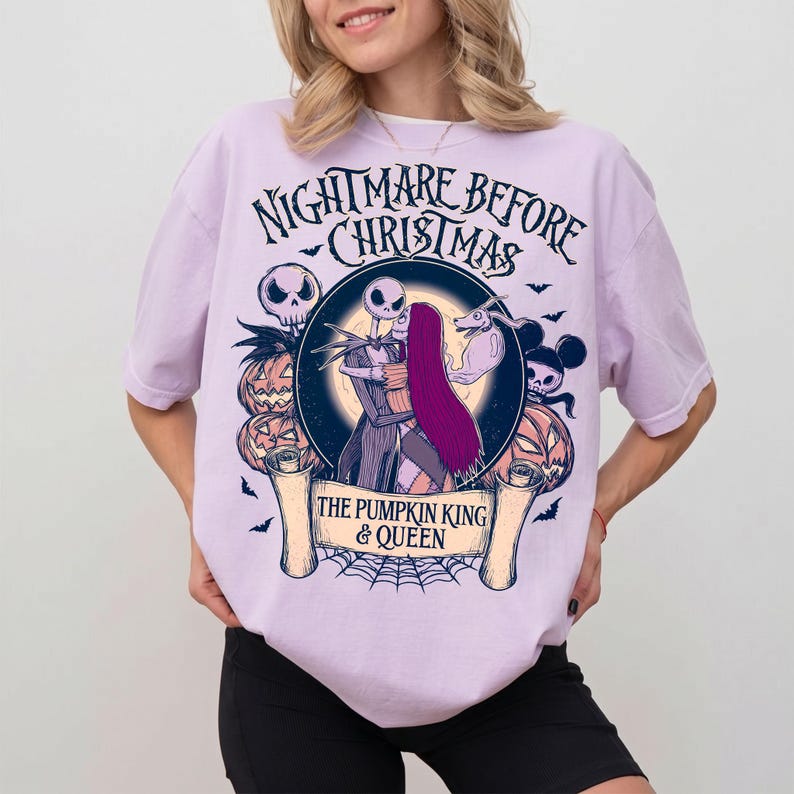 May include: A lilac t-shirt with a graphic from "The Nightmare Before Christmas." The design features Jack and Sally, pumpkins, bats, and the text "The Pumpkin King & Queen."