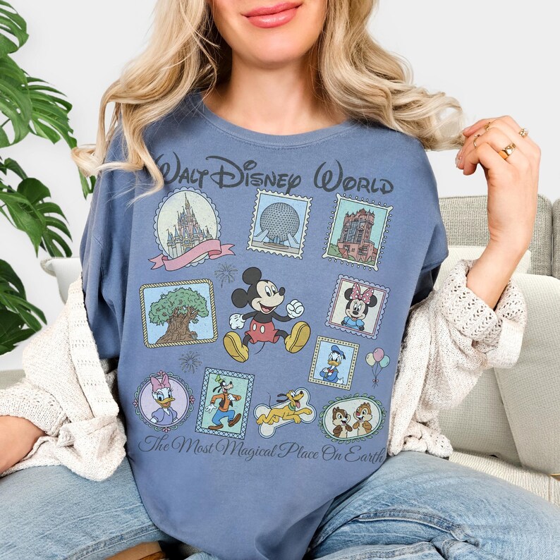 May include: A blue t-shirt featuring a collection of Disney-themed postage stamp designs. The stamps include images of Mickey Mouse, Minnie Mouse, Donald Duck, Goofy, and Chip and Dale, along with iconic park landmarks. Text reads "Walt Disney World" and "The Most Magical Place On Earth."