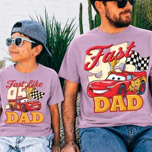 May include: Two matching light purple t-shirts. One shirt says "Fast like 05 Dad" with a cartoon race car and checkered flag. The other shirt says "Fast Dad" with a cartoon race car and checkered flag.