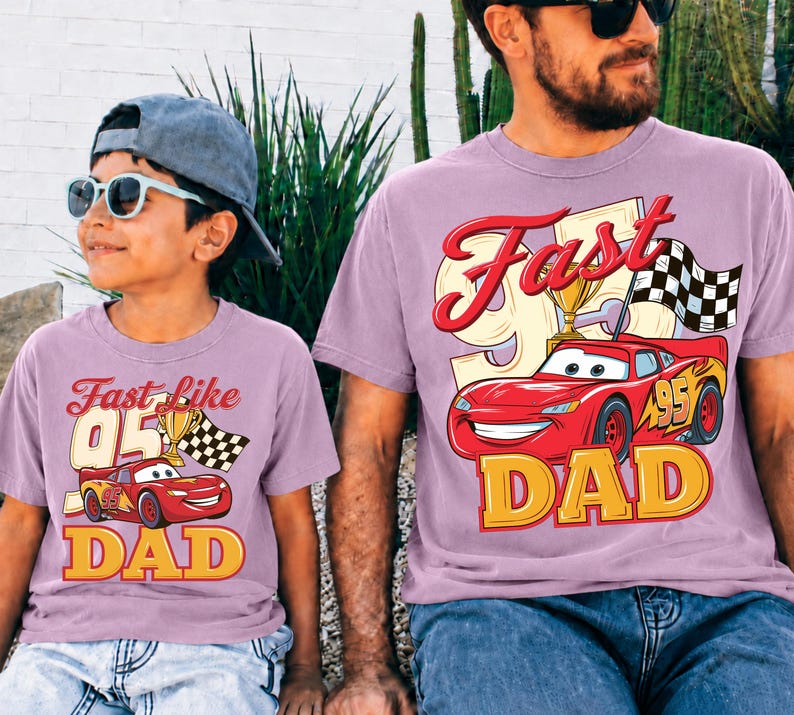 May include: Two matching light purple t-shirts. One shirt says "Fast like 05 Dad" with a cartoon race car and checkered flag. The other shirt says "Fast Dad" with a cartoon race car and checkered flag.