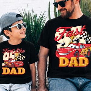 May include: Two black t-shirts with a red and yellow graphic of a race car and the words "Fast Dad" and "Fast like 95 Dad". The shirts are worn by a father and son, both wearing sunglasses.