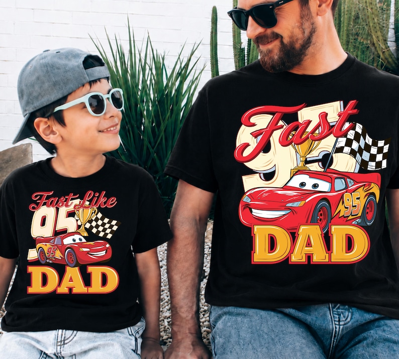 May include: Two black t-shirts with a red and yellow graphic of a race car and the words "Fast Dad" and "Fast like 95 Dad". The shirts are worn by a father and son, both wearing sunglasses.