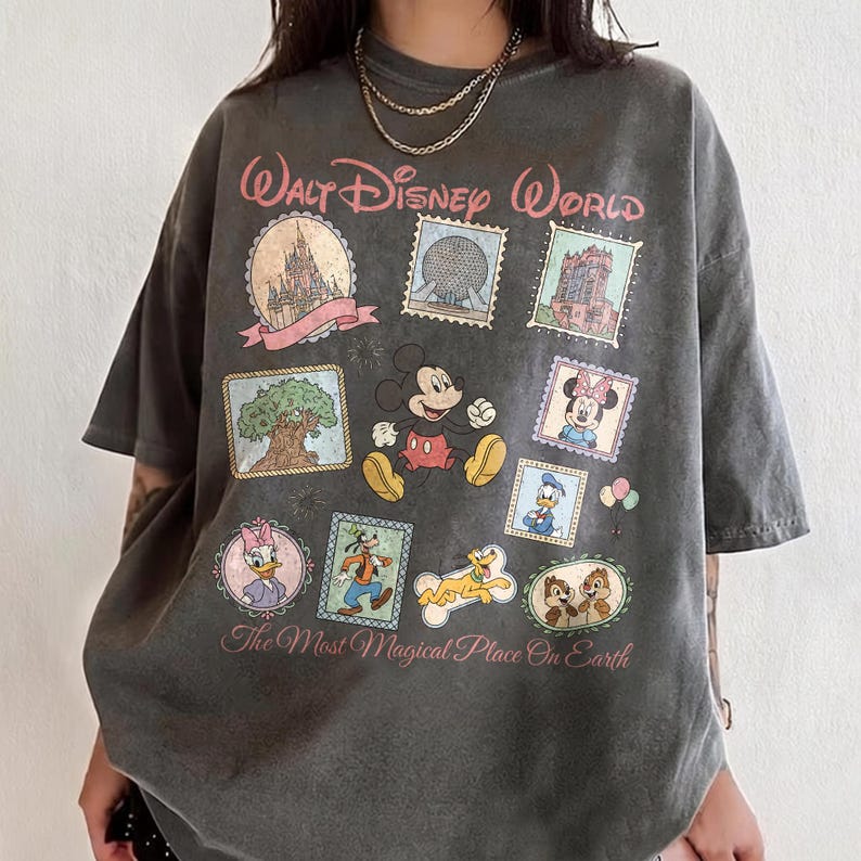 May include: Dark gray t-shirt featuring a Walt Disney World design. The design includes stamps with images of Mickey Mouse, Minnie Mouse, Donald Duck, Goofy, and Chip and Dale. The text "Walt Disney World" and "The Most Magical Place On Earth" are also included.