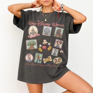 May include: Dark gray t-shirt featuring a colorful graphic of Mickey Mouse and other Disney characters. The shirt has the text "Walt Disney World" and "The Most Magical Place On Earth" in pink.