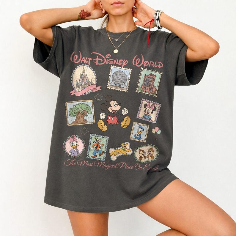 May include: Dark gray t-shirt featuring a colorful graphic of Mickey Mouse and other Disney characters. The shirt has the text "Walt Disney World" and "The Most Magical Place On Earth" in pink.