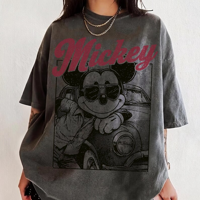 May include: Gray t-shirt featuring a graphic of Mickey Mouse wearing sunglasses and leaning against a car. The word "Mickey" is printed in red above the graphic. The shirt has short sleeves and a relaxed fit.