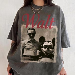 May include: Grey t-shirt with a vintage image of Walt Disney and Mickey Mouse wearing sunglasses. The word "Walt" is printed in red above the image. The shirt has short sleeves and a relaxed fit.