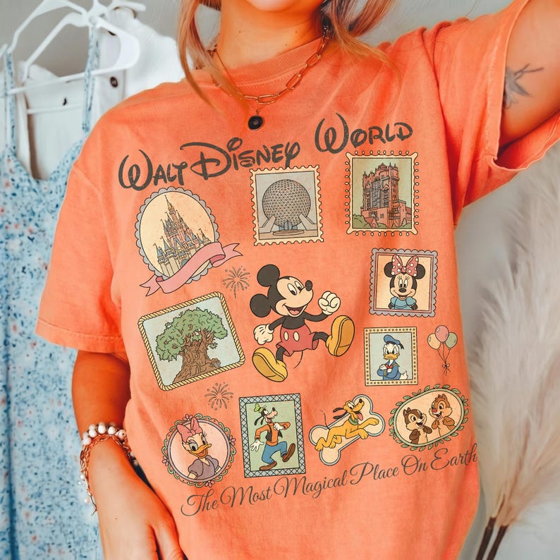 May include: Orange t-shirt with a Walt Disney World graphic. The design features Mickey Mouse, Minnie Mouse, Donald Duck, Goofy, Pluto, Chip and Dale, and other Disney park icons. The text "Walt Disney World" and "The Most Magical Place On Earth" are also visible.