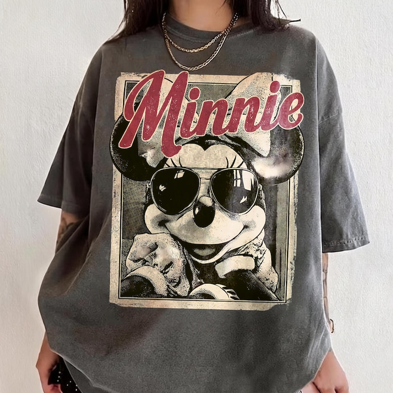 May include: Gray oversized t-shirt featuring a vintage graphic of Minnie Mouse wearing sunglasses. The word "Minnie" is printed in red script above the image. The shirt has short sleeves and a relaxed fit.