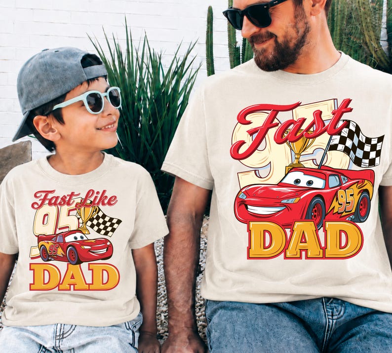 May include: Two matching beige t-shirts with the text "Fast Like 95 Dad" and a cartoon image of a red race car. The shirts are worn by a father and child, both wearing sunglasses.