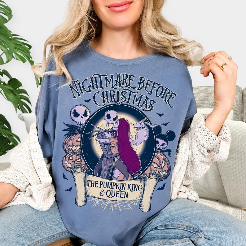 May include: A blue t-shirt with a graphic from "The Nightmare Before Christmas." The design shows Jack and Sally embracing, with pumpkins, bats, and the text "The Pumpkin King & Queen."