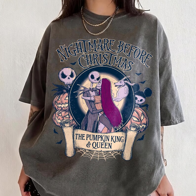 May include: Dark grey t-shirt with a graphic from "The Nightmare Before Christmas." The design features Jack and Sally, pumpkins, skulls, and the text "Nightmare Before Christmas" and "The Pumpkin King & Queen."