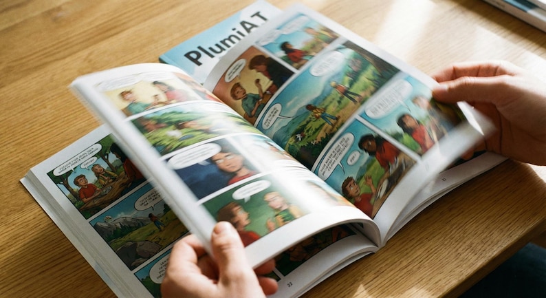 May include: Open comic book with colorful panels and speech bubbles. The cover of the book, titled "PlumiAT", is visible in the background. The pages are being turned, revealing sequential art with characters in various scenes.