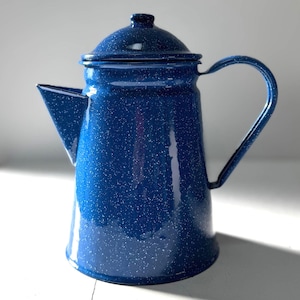 May include: A blue enamelware coffee pot with a lid and handle. The pot has a speckled pattern and a spout for pouring. The pot is designed for camping or outdoor use.