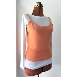 May include: An orange camisole with thin straps and a ribbed bottom layer is layered over a white long-sleeve shirt. The camisole has a scalloped neckline. The clothing is displayed on a brown dress form.