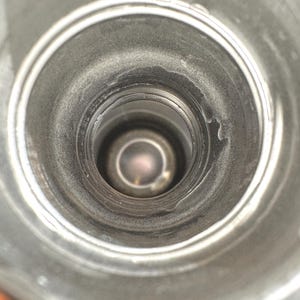 May include: A top-down view into the cylindrical opening of a metallic bottle. The interior walls are smooth and silver-toned, leading down to a circular base. The rim of the opening features a threaded neck design for a cap, with a metallic finish.
