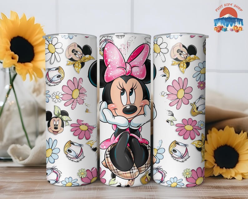 May include: A white tumbler featuring Minnie Mouse in a pink dress and bow, surrounded by cartoon flowers and character faces. The tumbler has a stainless steel appearance and is decorated with a repeating pattern of daisies and other floral elements.