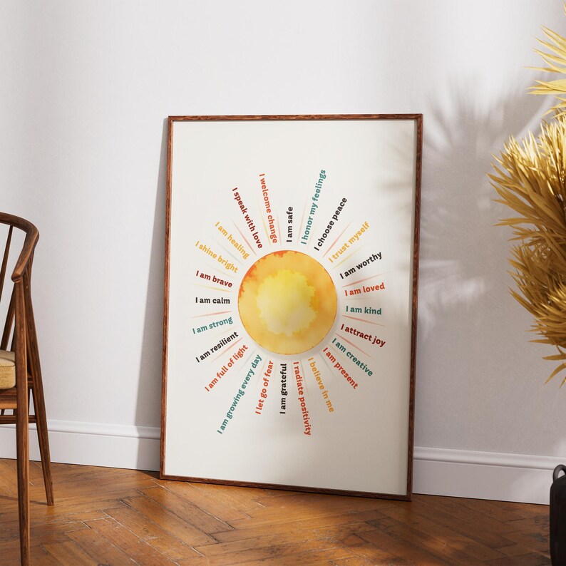 May include: A framed art print with a watercolor sun design and affirmations in a circular pattern. The affirmations include phrases like "I am brave," "I am loved," and "I choose peace." The print is in a wooden frame.