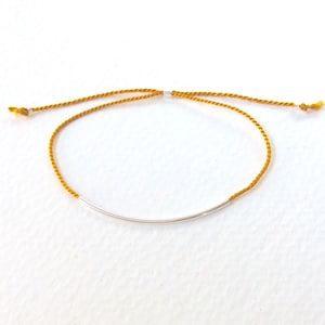 May include: A yellow braided cord bracelet with a silver bar accent.
