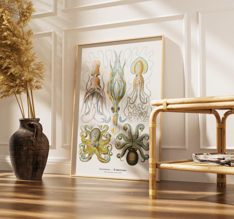 May include: A framed vintage print featuring detailed illustrations of various cephalopods in shades of brown, blue, and green. The print is displayed in a light-colored wooden frame, leaning against a white wall. A dark vase with dried plants and a bamboo side table are in the foreground.