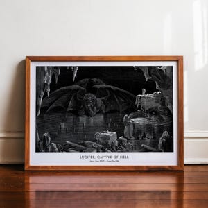 Peut inclure: Une impression encadrée en noir et blanc d'une illustration détaillée représentant Lucifer dans un cadre caverneux. L'œuvre présente une grande figure ailée et le texte "LUCIFER. CAPTIVE OF HELL". L'impression est encadrée dans un cadre en bois.