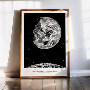 Peut inclure: Une impression encadrée en noir et blanc de la Terre vue de la Lune. L'œuvre présente une illustration détaillée de la Lune et de la Terre sur un fond étoilé. Le texte en bas indique "THE EARTH AS SEEN FROM THE MOON".