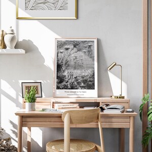 May include: A light wood desk with a framed print of a black and white illustration. The print has the text "Prince Roumanie & Ile Crepo". A small potted plant, books, and a gold desk lamp are also on the desk.